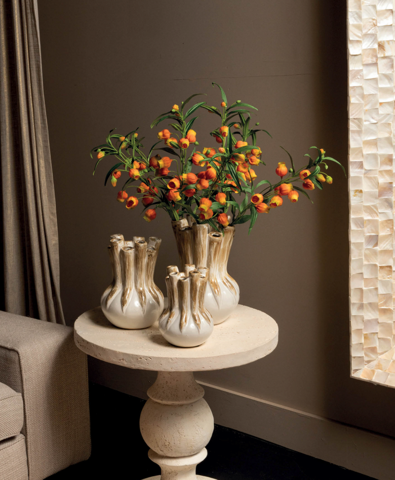Een sfeervol gestylede hoek met drie ambachtelijke tulpenvazen in glanzend keramiek, gevuld met kleurrijke bloesems op een sculpturale stenen bijzettafel, weerspiegelt de zorgvuldige aandacht voor detail en persoonlijke styling.