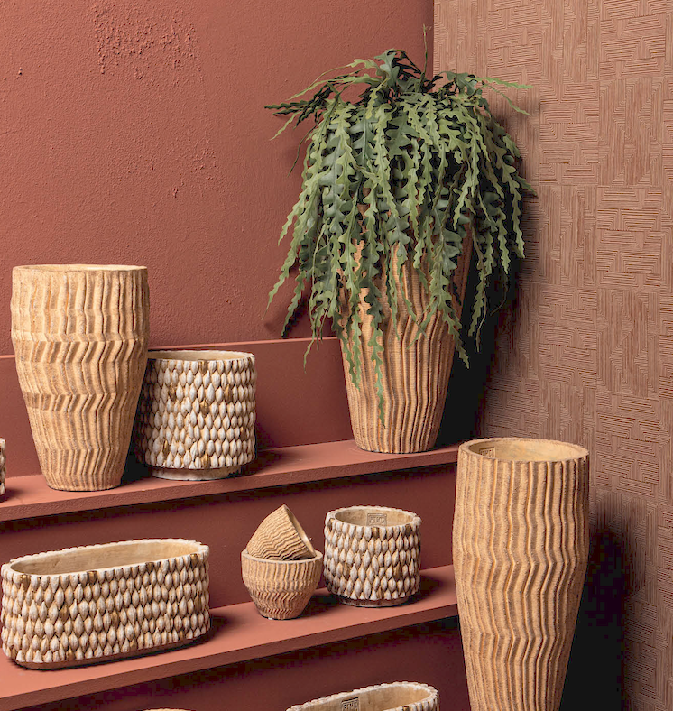 Een zorgvuldig gecureerde presentatie van ambachtelijke keramieken plantenpotten en vazen met voelbare reliëfstructuren en een hangplant, tentoongesteld tegen een warme terracotta wand als uiting van karakter en bezieling.